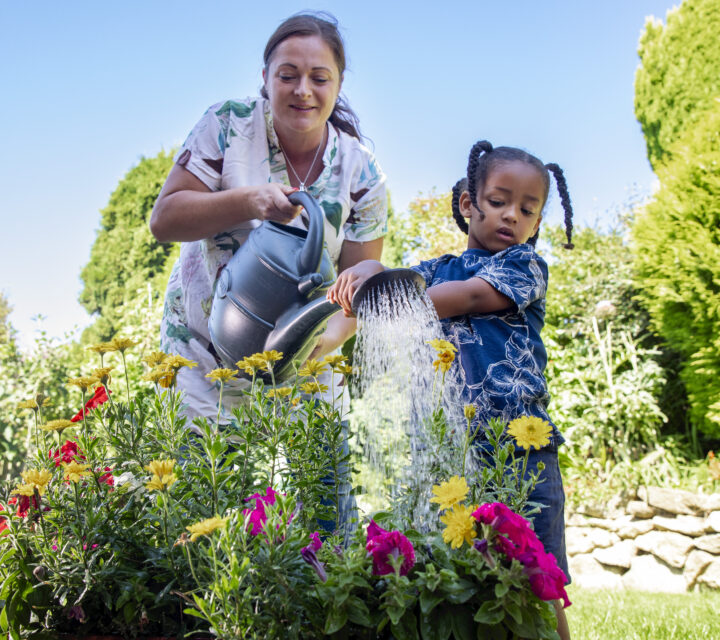 woman and child watering plants in garden with watering can